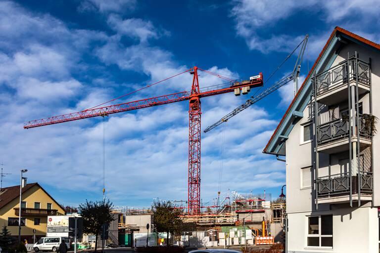 Eine Hausbaustelle mit einem roten Kran vor blauem, leicht bewölktem Himmel.