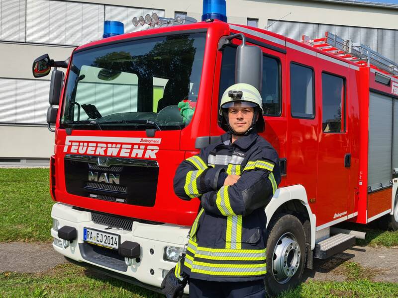 Feuerwehrmann mit Helm vor einem Hilfeleistungslöschgruppenfahrzeug